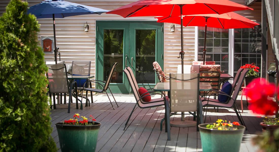 Wooden deck with several patio umbrella tables and chairs and potted red flowers