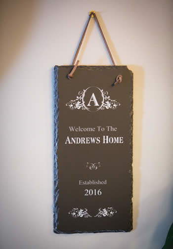 Brown sign hanging from a leather strap that says Welcome To The Andrews Home Established 2016