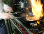 Close up view of a person’s hands cooking on a stove with flames in an iron skillet