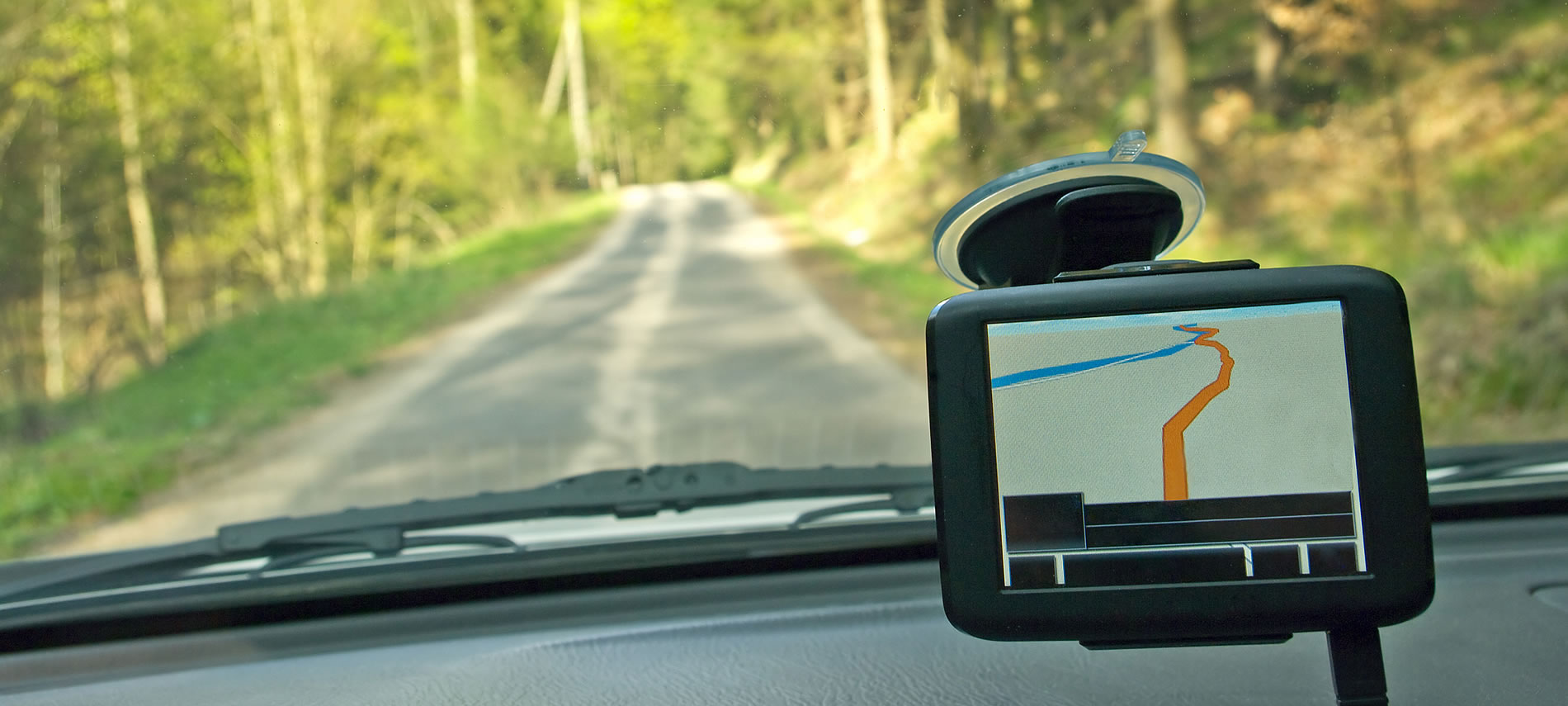 View through a windshield and GPS and a rolling road ahead surrounded by green trees