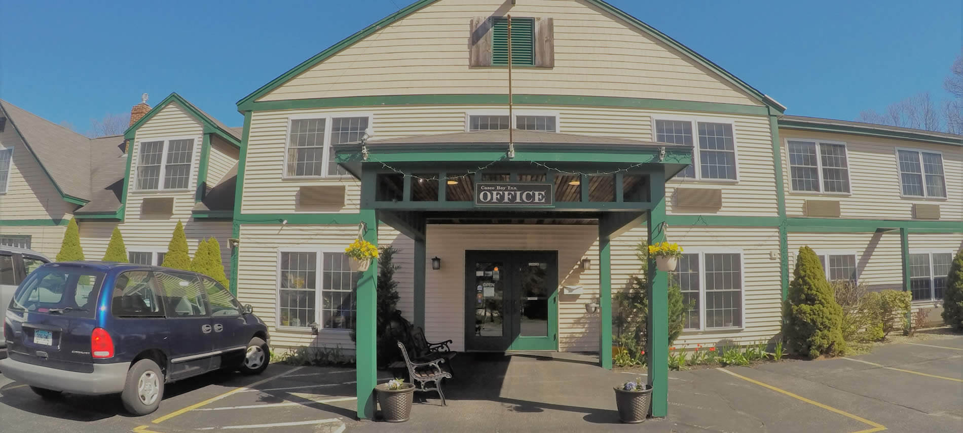  Two story tan building with green trim, gable room, green painted portico, double glass doors and an OFFICE sign