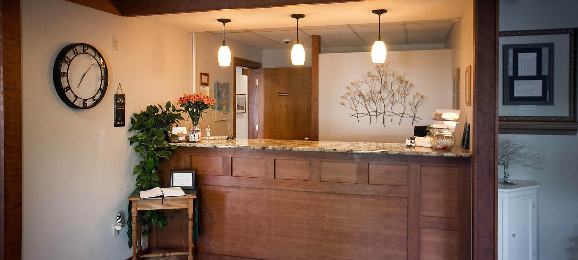 Wood stained welcome counter topped with fresh flowers and three hanging pendant lights