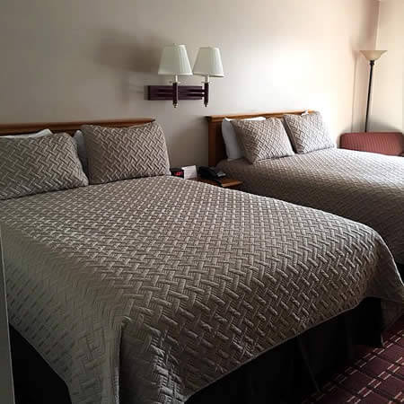 Beige room with two beds topped with tan basket weave patterned bedding and a double light wall sconce
