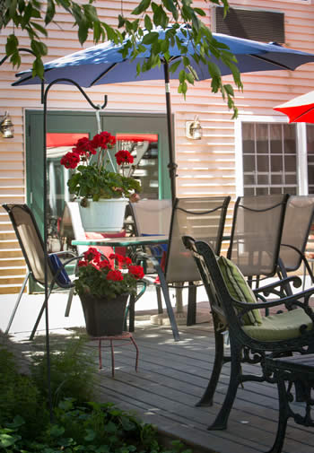 Wooden deck with several patio umbrella tables and chairs and potted red flowers