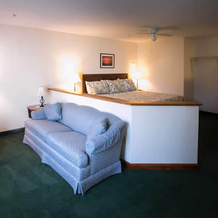 White room with green carpet, a bed with floral bedding, and a blue sofa